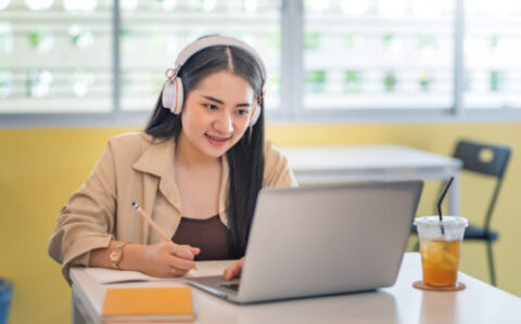 Young Asian woman wearing headphones takes notes and learn onlin